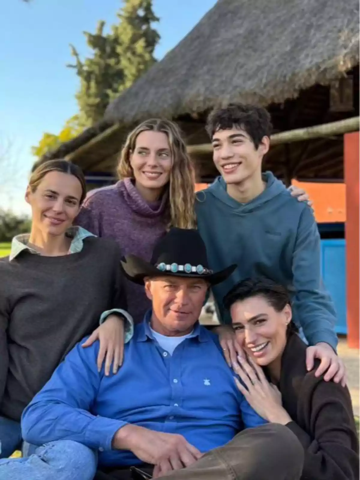 Un grupo de cinco personas posando juntas al aire libre, con un hombre en el centro usando un sombrero de vaquero y las demás personas sonriendo a su alrededor. Un grupo de cinco personas posando juntas al aire libre, con un hombre en el centro usando un sombrero de vaquero y las demás personas sonriendo a su alrededor.