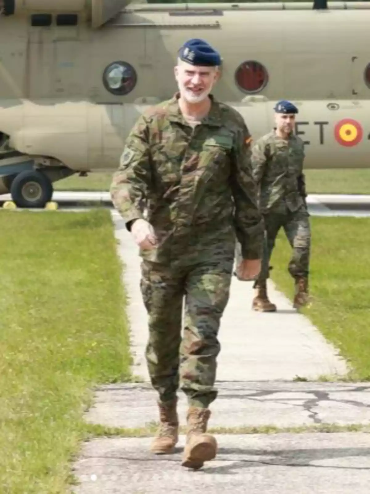 Felipe VI and another man in camouflage uniform and a blue beret walk along a concrete runway with a military helicopter in the background. Felipe VI and another man in camouflage uniform and a blue beret walk along a concrete runway with a military helicopter in the background.
