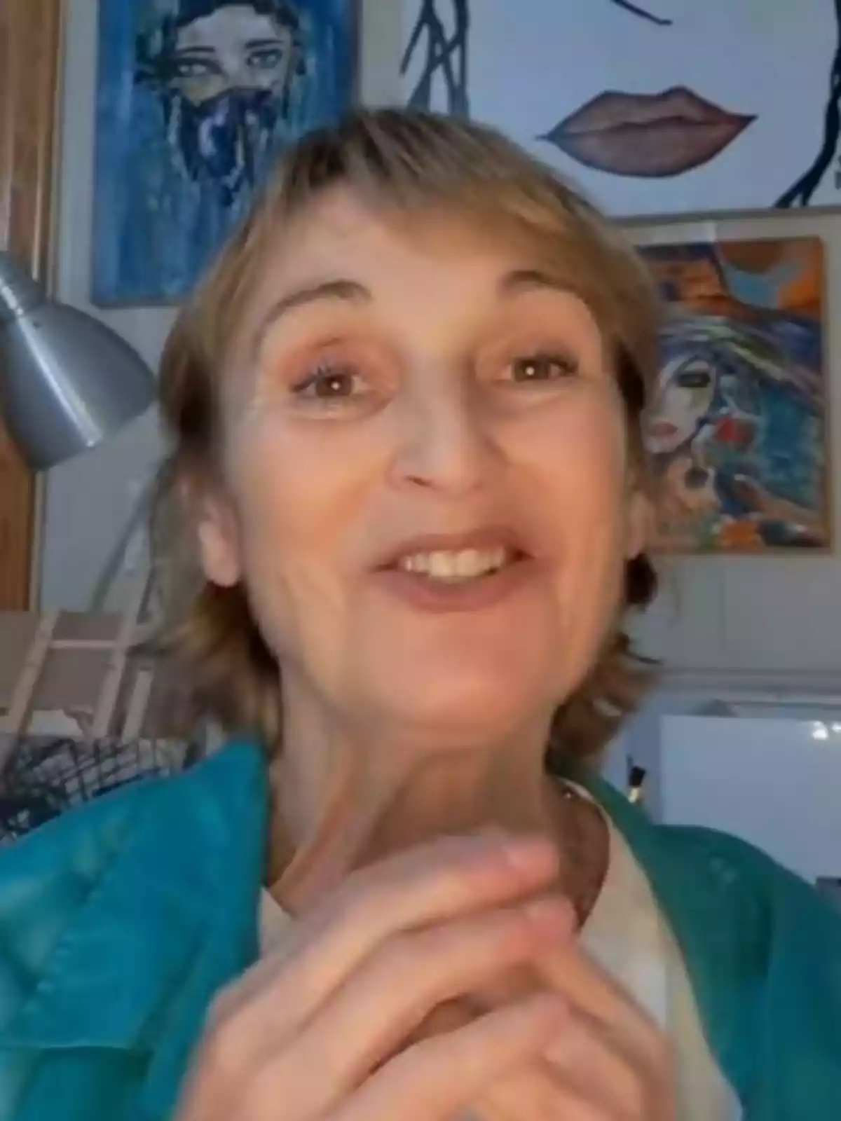 Cristina Fenollar sonriente con cabello corto y rubio, vestida con una chaqueta azul, en una habitación con varias pinturas coloridas en la pared de fondo. Cristina Fenollar sonriente con cabello corto y rubio, vestida con una chaqueta azul, en una habitación con varias pinturas coloridas en la pared de fondo.