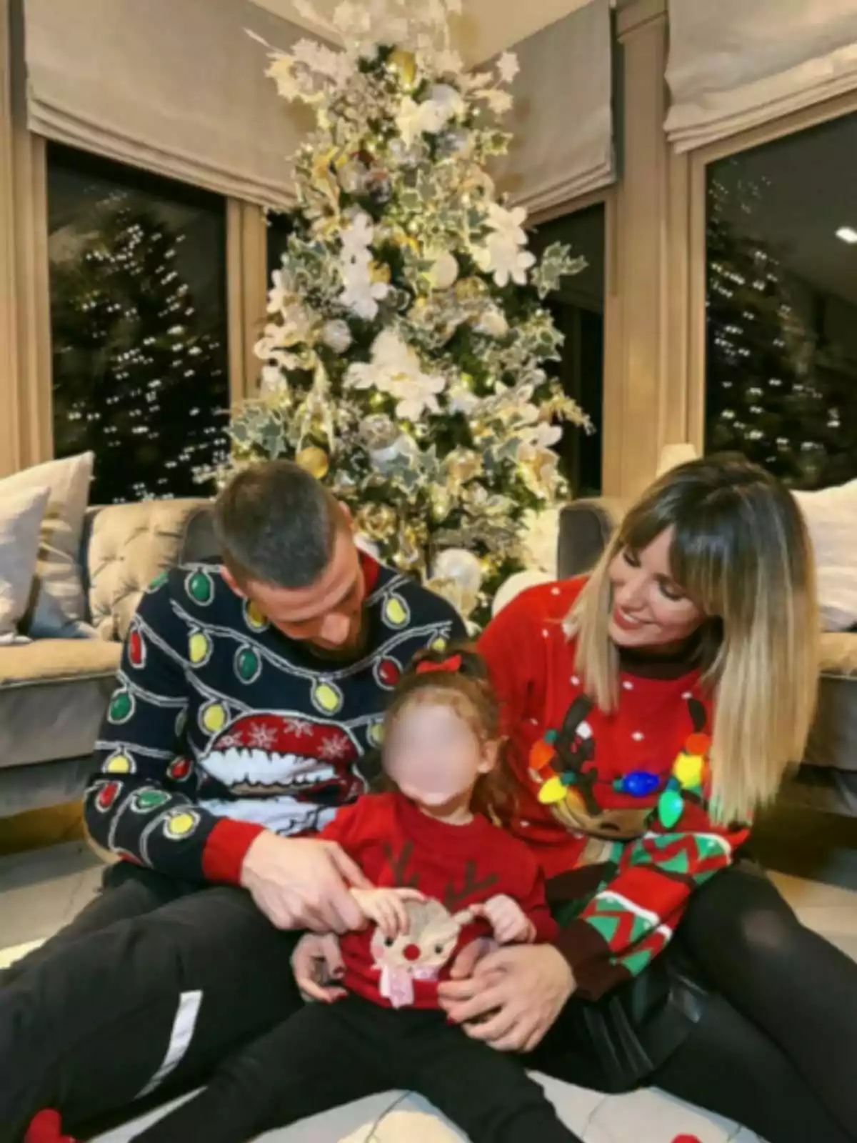 Familia sentada frente a un árbol de Navidad decorado, usando suéteres navideños y sonriendo juntos Familia sentada frente a un árbol de Navidad decorado, usando suéteres navideños y sonriendo juntos