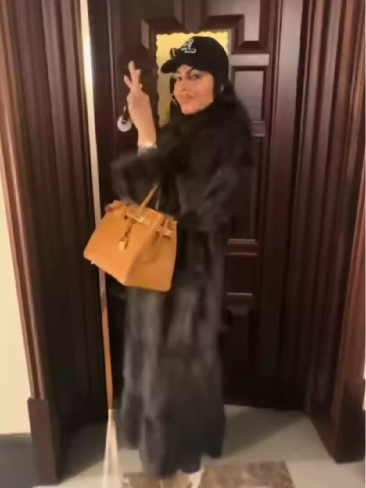 Georgina Rodríguez con abrigo oscuro y gorra negra posando frente a una puerta de madera mientras sostiene un bolso marrón y hace el signo de paz con la mano Georgina Rodríguez con abrigo oscuro y gorra negra posando frente a una puerta de madera mientras sostiene un bolso marrón y hace el signo de paz con la mano
