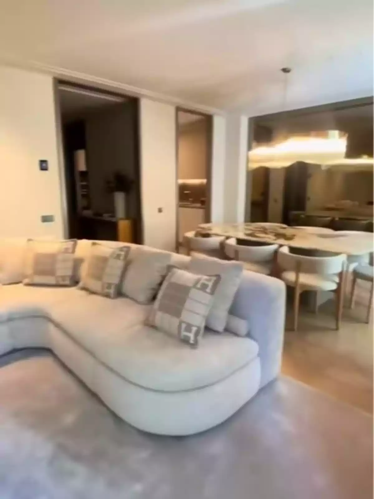 Sala moderna con sofá en forma de L color claro cojines decorativos mesa de comedor con varias sillas y lámpara colgante Sala moderna con sofá en forma de L color claro cojines decorativos mesa de comedor con varias sillas y lámpara colgante