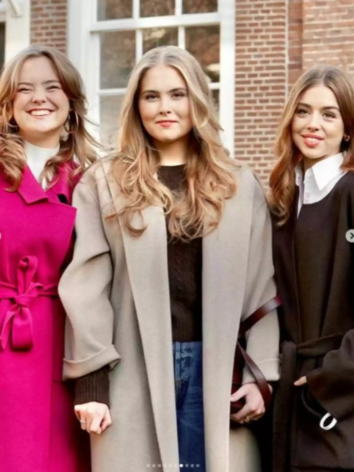Ariane, Amalia y Alexia de Holanda posan juntas al aire libre, vistiendo abrigos elegantes y sonriendo frente a un edificio de ladrillo con ventanas grandes. Ariane, Amalia y Alexia de Holanda posan juntas al aire libre, vistiendo abrigos elegantes y sonriendo frente a un edificio de ladrillo con ventanas grandes.