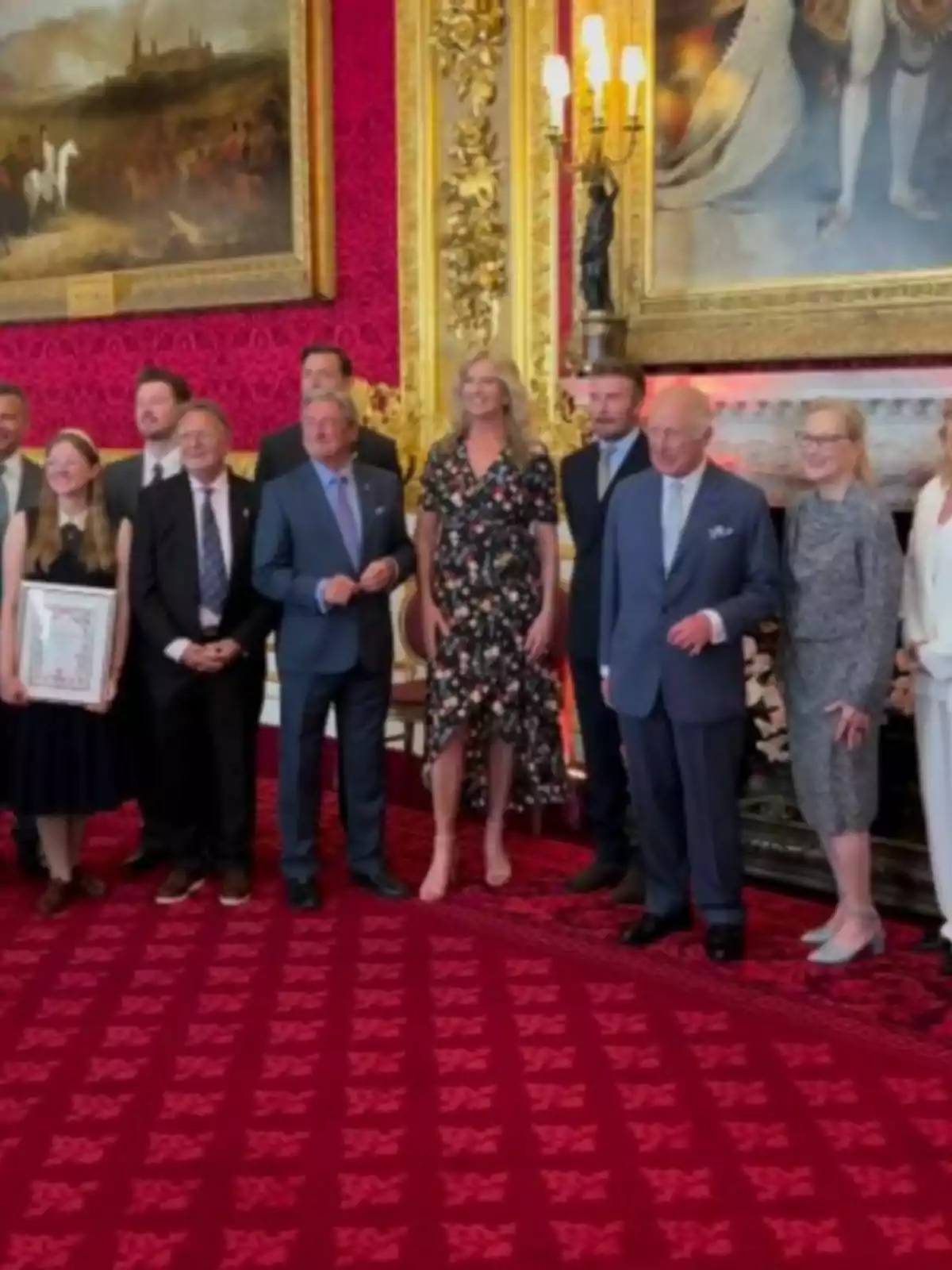 Un grupo de personas elegantemente vestidas posando en una lujosa sala con alfombra roja, paredes decoradas en dorado y cuadros grandes al fondo Un grupo de personas elegantemente vestidas posando en una lujosa sala con alfombra roja, paredes decoradas en dorado y cuadros grandes al fondo
