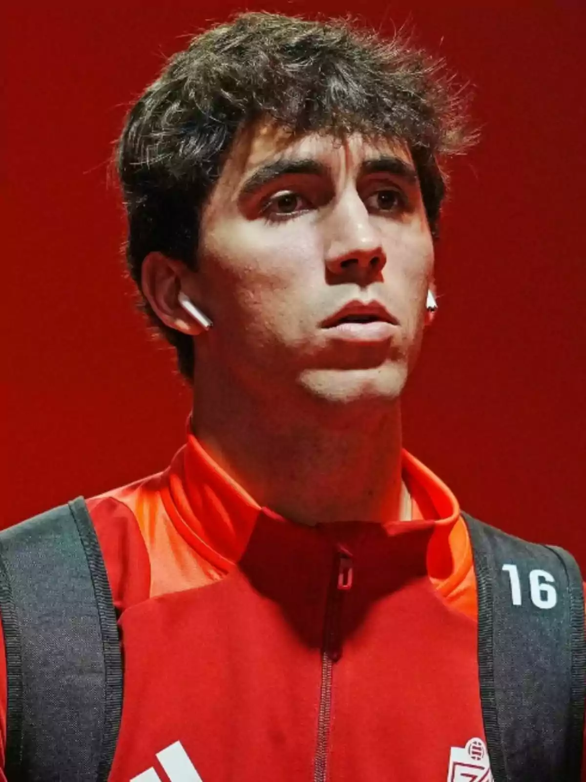 Manu Lama con auriculares y chaqueta roja con el número 16 en un fondo rojo. Manu Lama con auriculares y chaqueta roja con el número 16 en un fondo rojo.