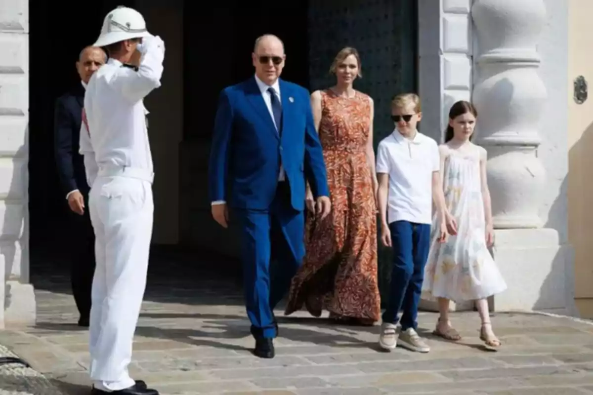 Una familia elegantemente vestida sale de un edificio mientras un guardia con uniforme blanco les saluda Una familia elegantemente vestida sale de un edificio mientras un guardia con uniforme blanco les saluda