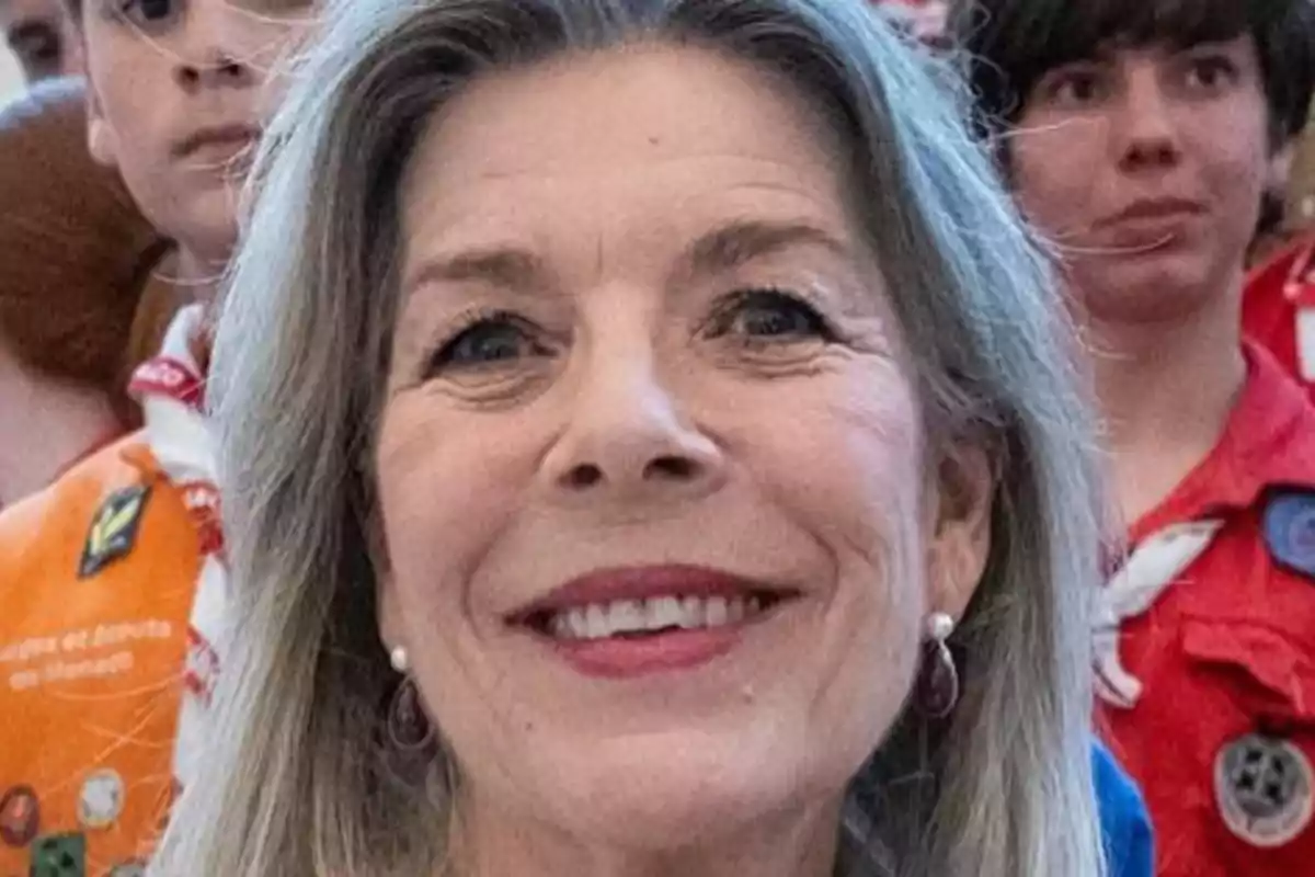 Carolina of Monaco smiling with gray hair and earrings, surrounded by people in scout uniforms.