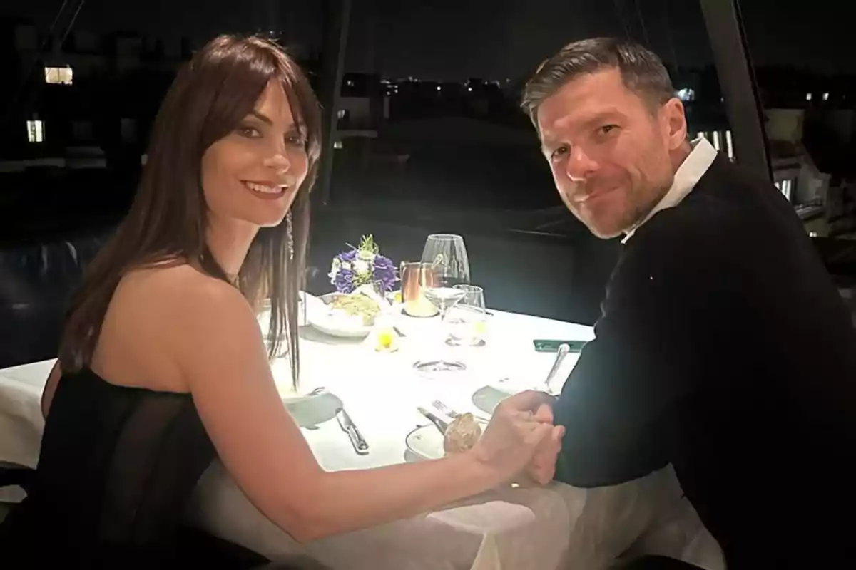Nagore Aranburu y Xabi Alonso sentada en una mesa de restaurante elegantemente decorada, sosteniéndose de las manos y sonriendo a la cámara. Nagore Aranburu y Xabi Alonso sentada en una mesa de restaurante elegantemente decorada, sosteniéndose de las manos y sonriendo a la cámara.