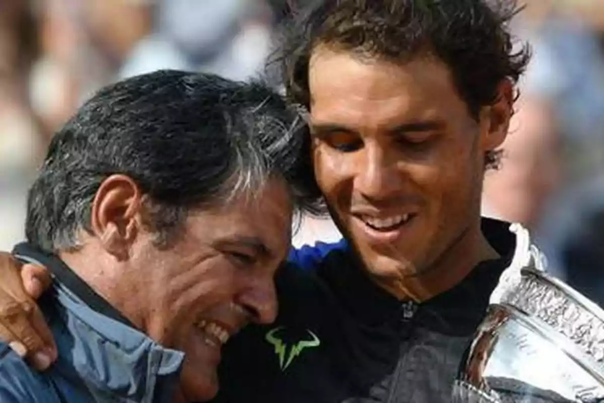 Toni y Rafa Nadal sonríen y se abrazan mientras una de ellas sostiene un trofeo plateado. Toni y Rafa Nadal sonríen y se abrazan mientras una de ellas sostiene un trofeo plateado.