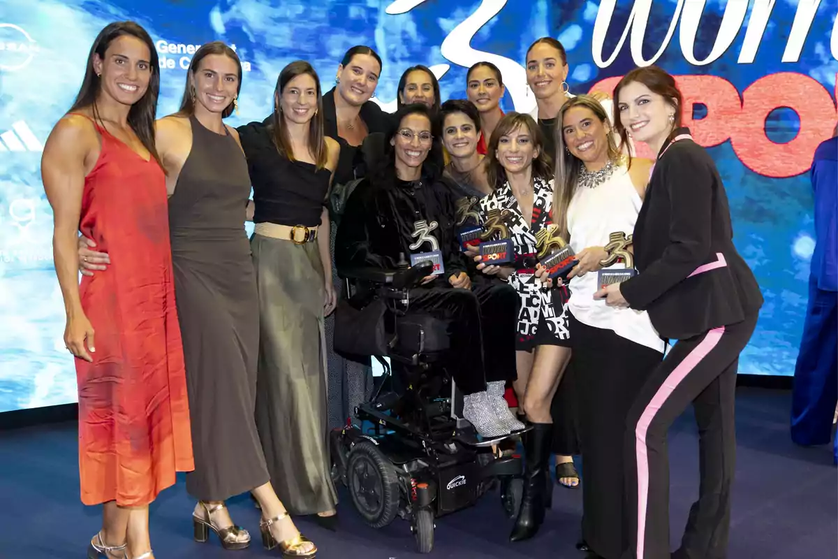 Un grupo de mujeres sonrientes posando juntas en un evento, algunas sostienen trofeos en sus manos.