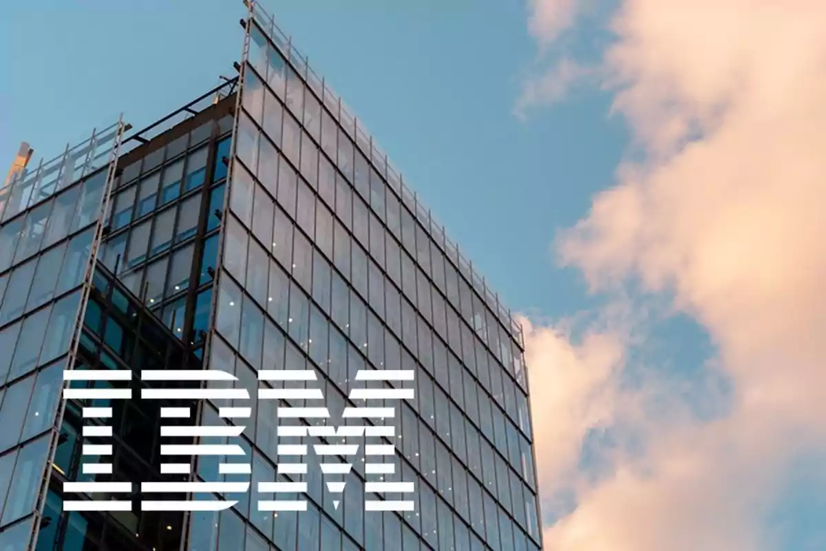 Modern glass building with the IBM logo against the blue sky with clouds.