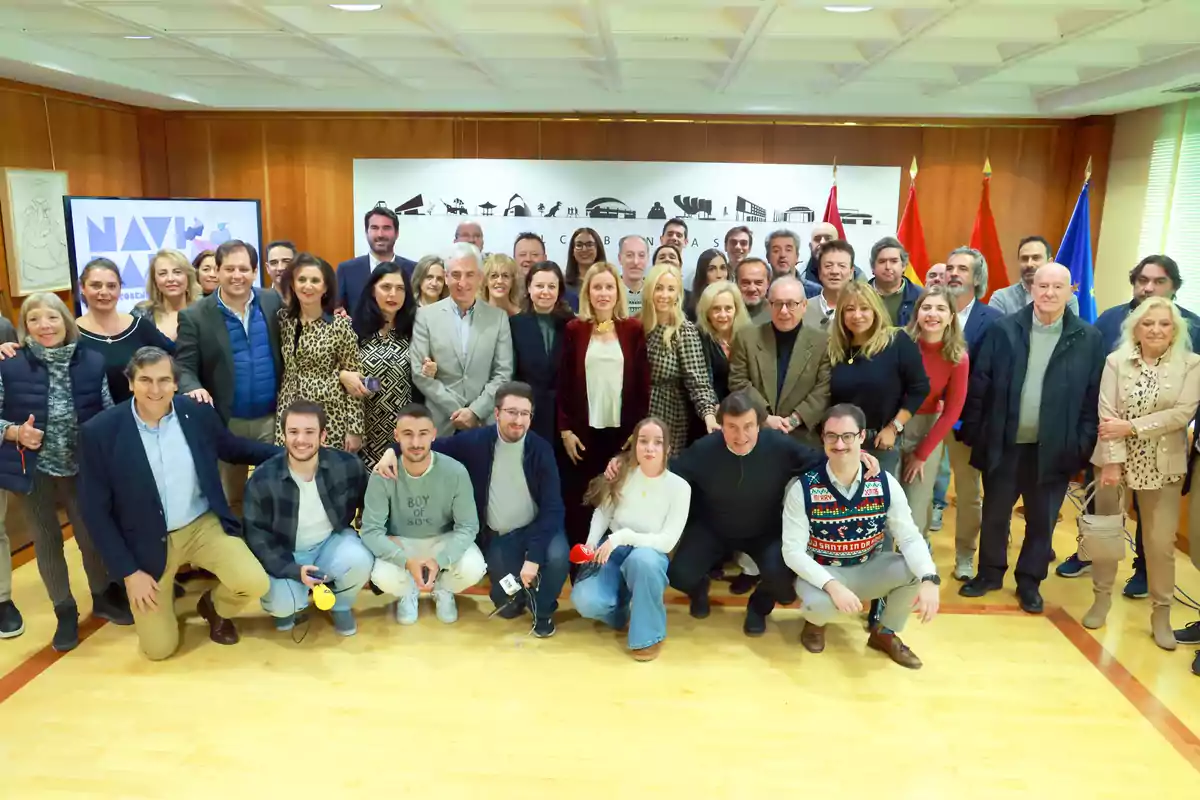 Un grupo numeroso de personas posando juntas en una sala con banderas y un cartel en la pared.