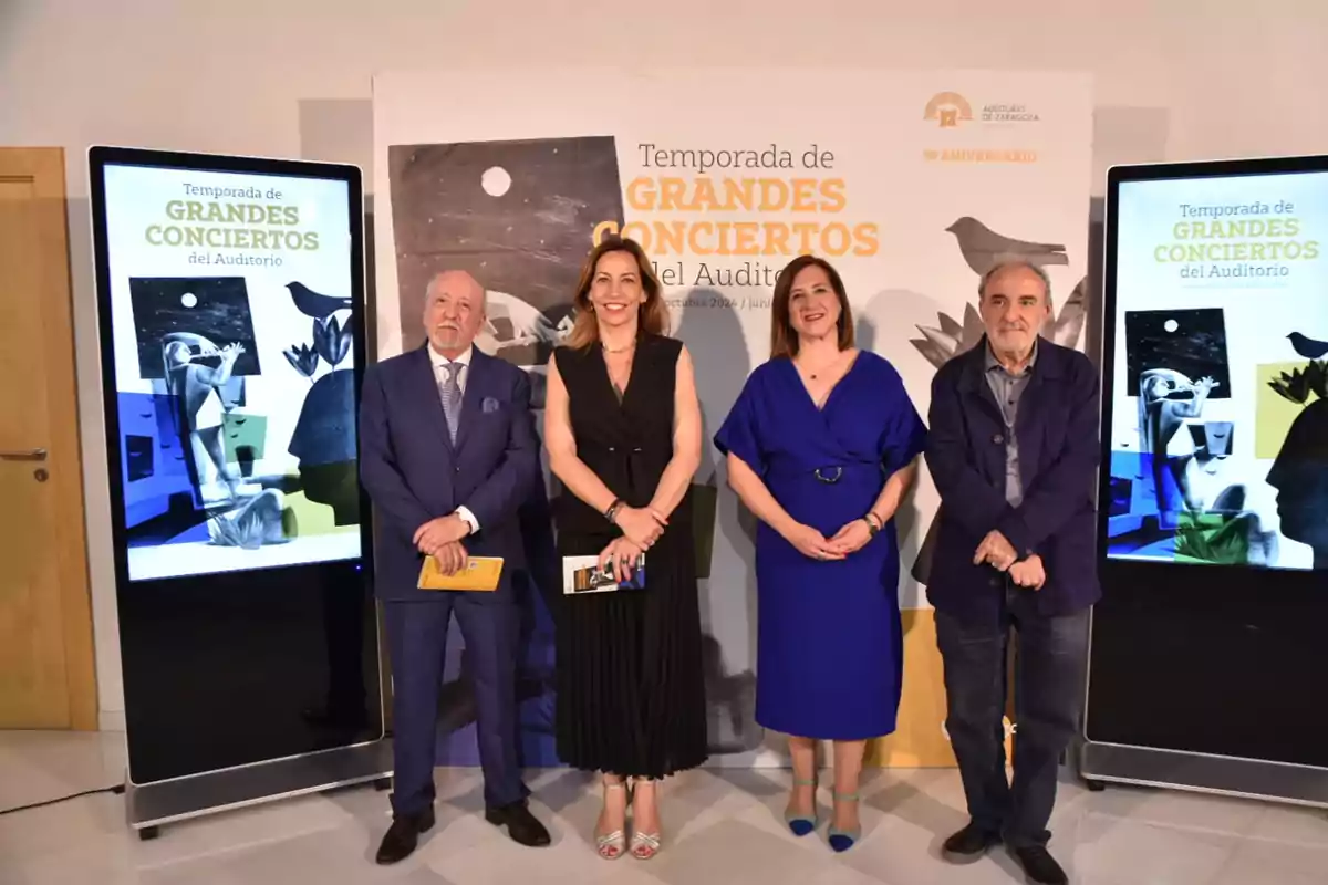 Personas posando frente a un cartel que anuncia la "Temporada de Grandes Conciertos del Auditorio" con dos pantallas a los lados mostrando la misma información.