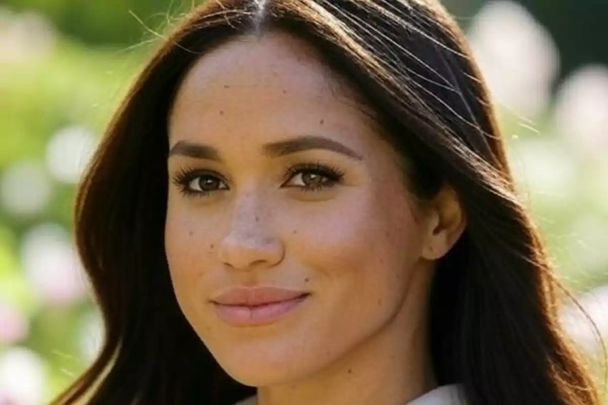 Close-up of Meghan Markle looking at the camera in a sunny outdoor setting.