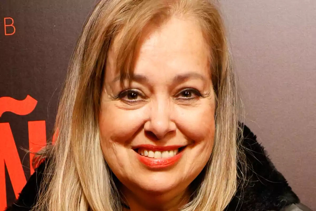 Emma Ozores sonriendo frente a un fondo oscuro con letras rojas.