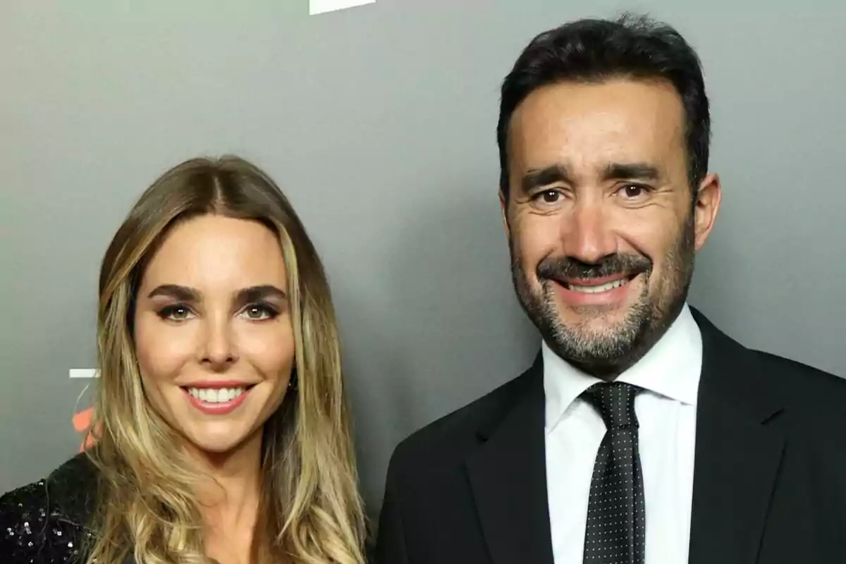 Helena Condis y Juanma Castaño sonriendo frente a una pared gris.