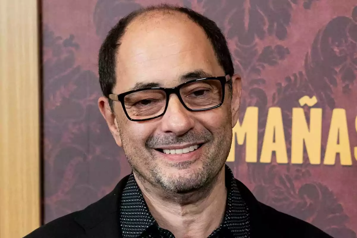 Jordi Sánchez con gafas y barba sonríe frente a un fondo decorativo.