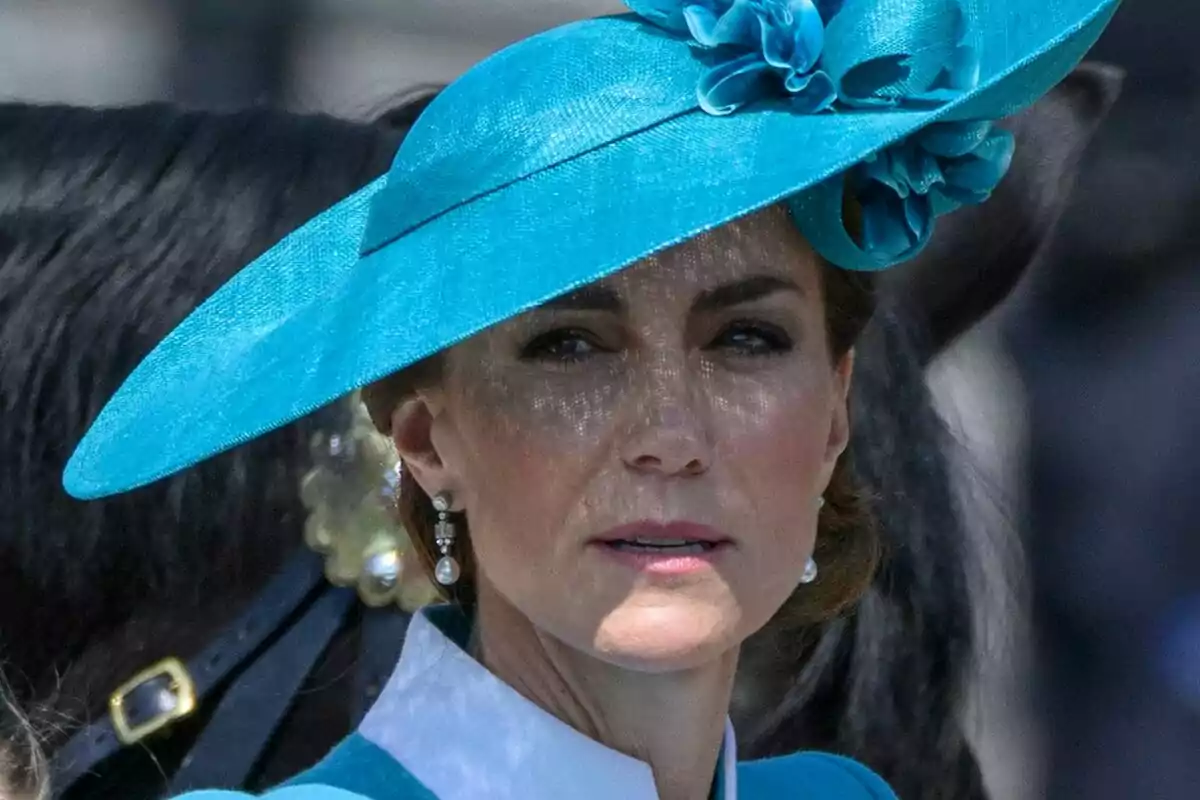 Woman wearing a blue hat decorated with flowers and pearl earrings, with a blurred background where part of a black horse can be seen