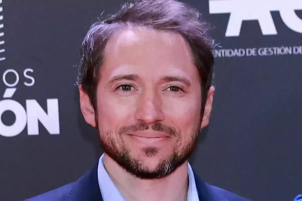 Manuel Martos con barba y cabello castaño sonríe frente a un fondo oscuro con texto blanco.