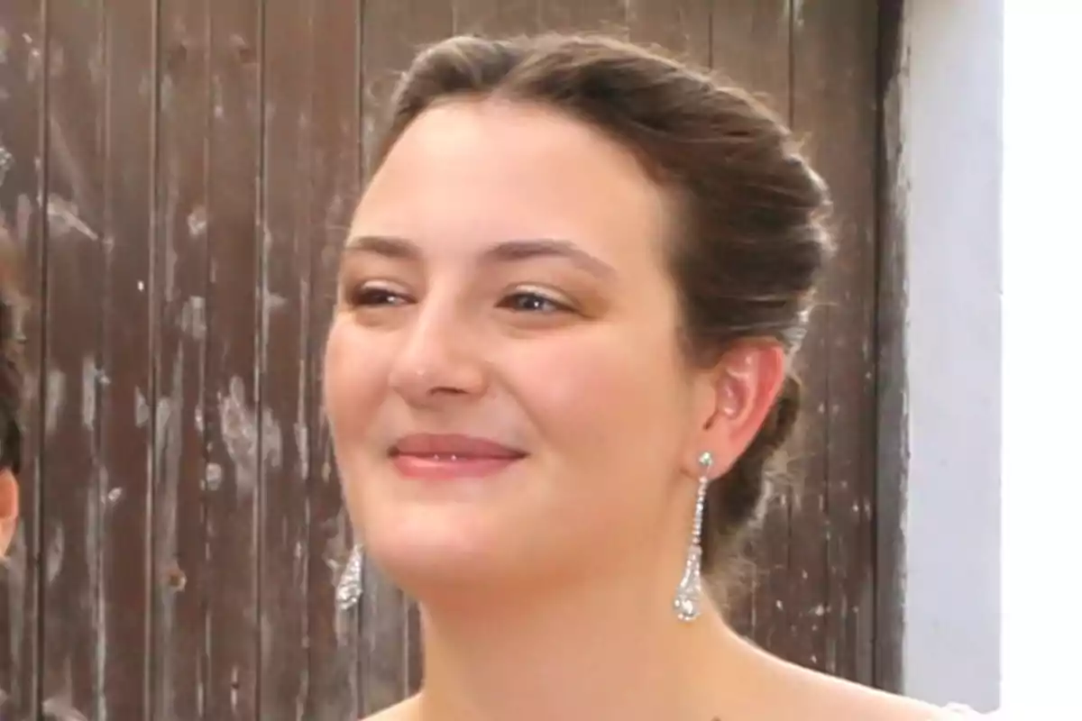 Victoria de Hohenlohe con el cabello recogido, usando aretes largos y brillantes, sonriendo frente a una puerta de madera Victoria de Hohenlohe con el cabello recogido, usando aretes largos y brillantes, sonriendo frente a una puerta de madera