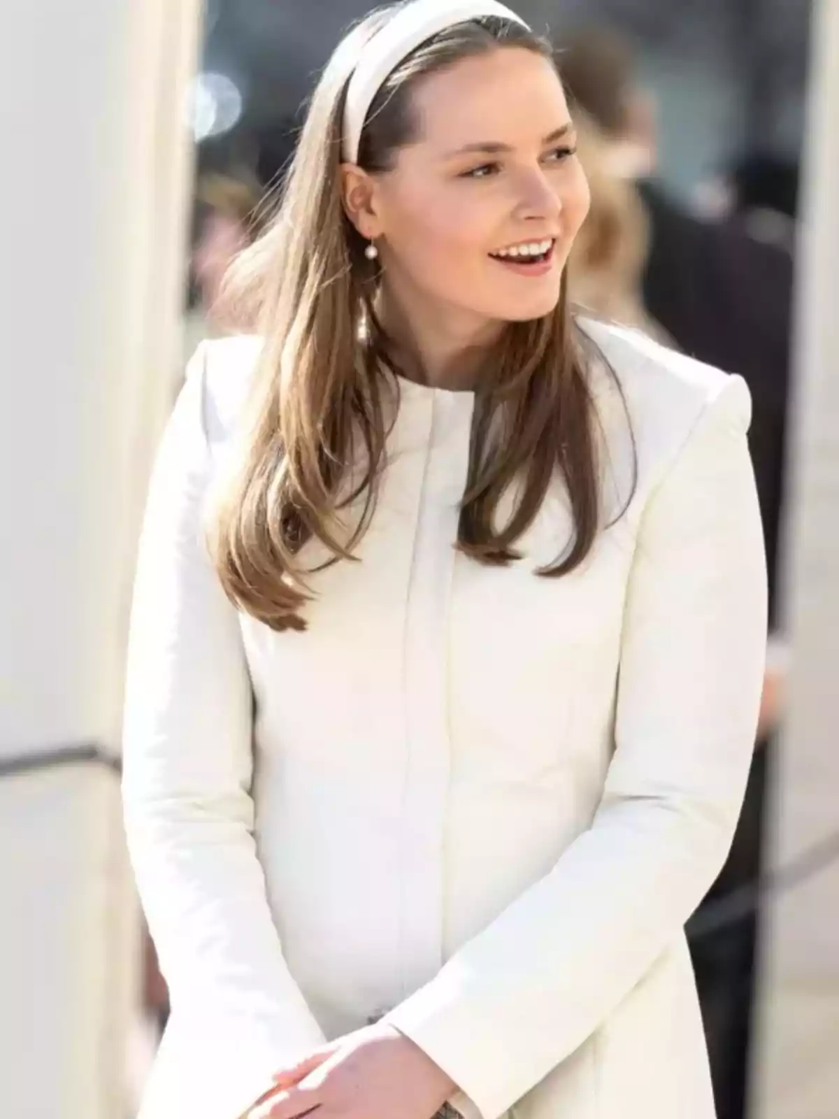 Young person with long, straight hair wears a white headband and a light-colored coat while smiling and looking to the side in an outdoor setting. Young person with long, straight hair wears a white headband and a light-colored coat while smiling and looking to the side in an outdoor setting.