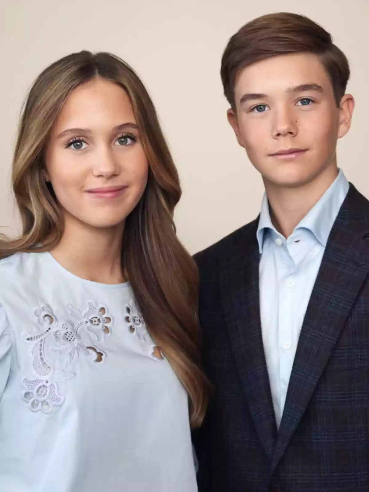 Two teenagers pose together looking at the camera; she is wearing a light blue embroidered blouse and he is dressed in a dark jacket and light-colored jersey. Two teenagers pose together looking at the camera; she is wearing a light blue embroidered blouse and he is dressed in a dark jacket and light-colored jersey.