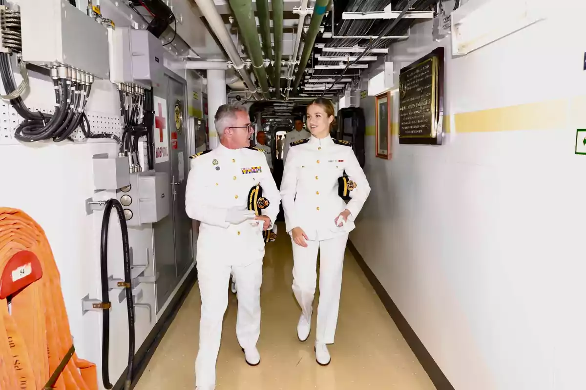 Leonor con uniforme blanco de gala de la marina camina por un pasillo de un barco mientras conversa y sonríe Leonor con uniforme blanco de gala de la marina camina por un pasillo de un barco mientras conversa y sonríe