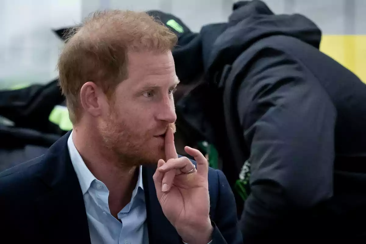 El príncipe Harry con barba hace un gesto de silencio con el dedo índice sobre los labios mientras lleva puesto un traje oscuro y una camisa clara. El príncipe Harry con barba hace un gesto de silencio con el dedo índice sobre los labios mientras lleva puesto un traje oscuro y una camisa clara.