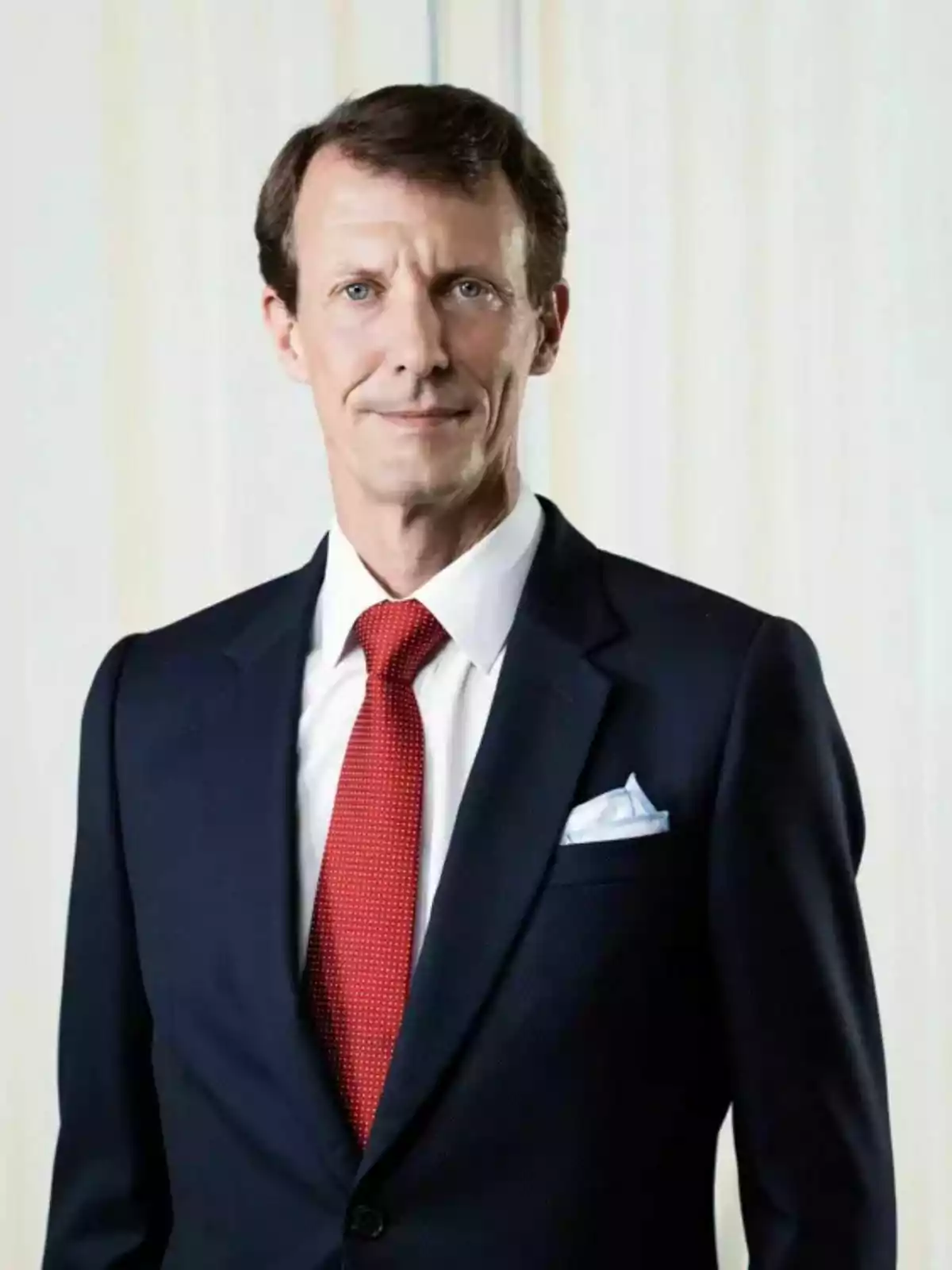 El príncipe Joaquín de Dinamarca vistiendo un traje azul marino con corbata roja y camisa blanca posando frente a un fondo claro El príncipe Joaquín de Dinamarca vistiendo un traje azul marino con corbata roja y camisa blanca posando frente a un fondo claro