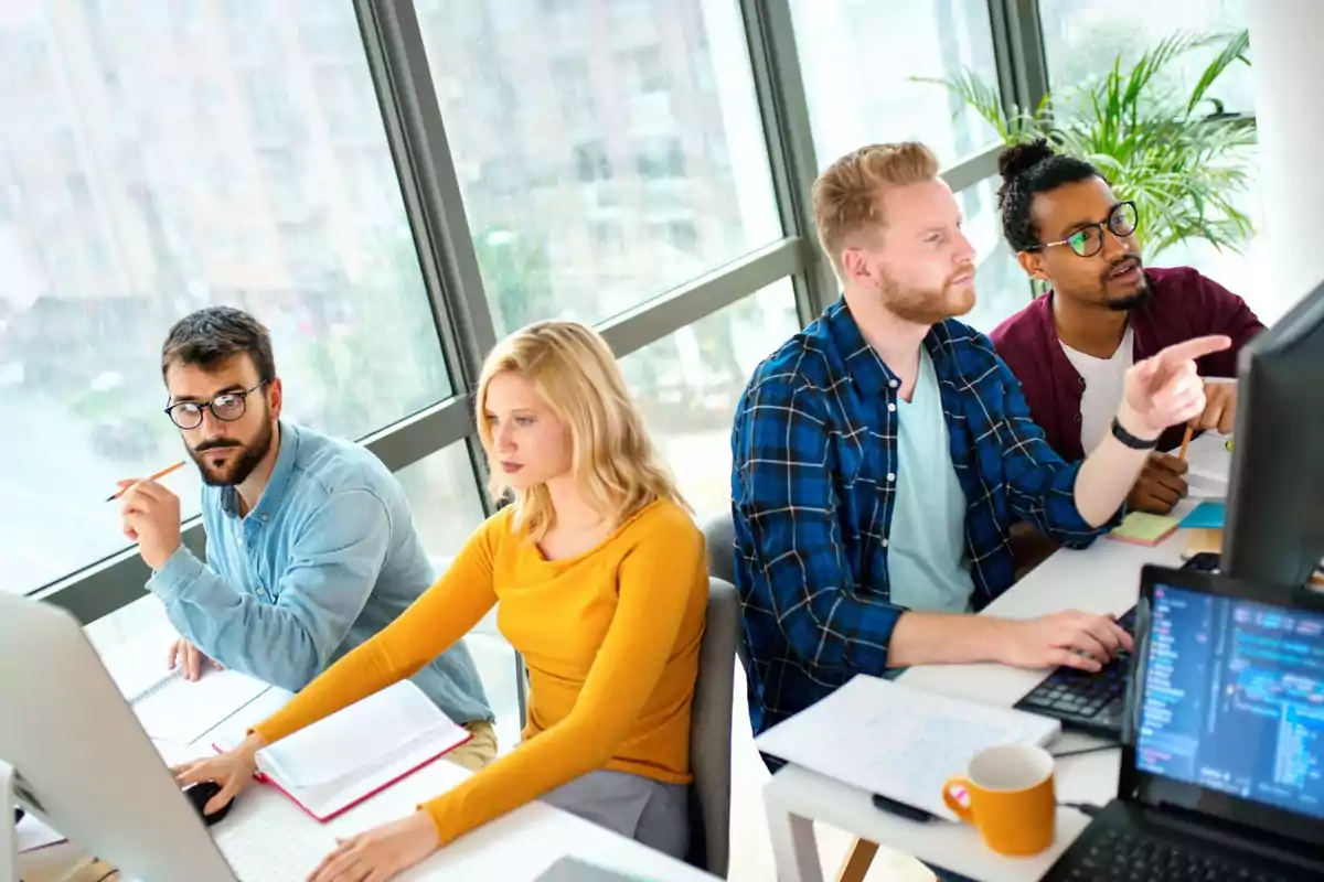 Grupo de personas trabajando en una oficina frente a computadoras.