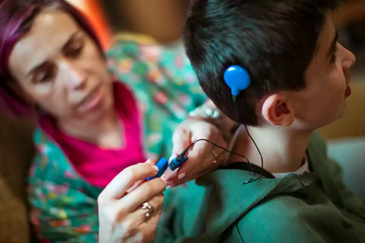 Una mujer ajusta un dispositivo auditivo en la cabeza de un niño.