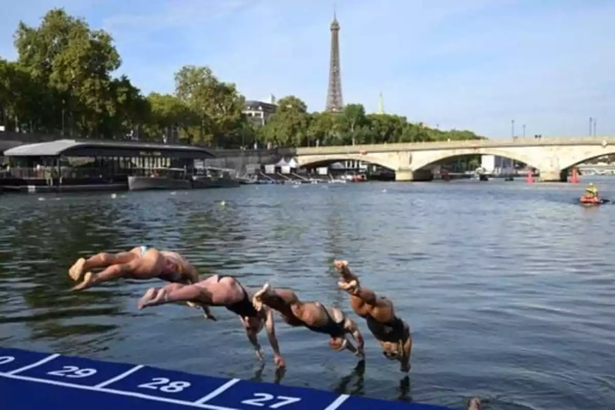 Personas saltando al agua desde una plataforma numerada con la Torre Eiffel y un puente de fondo.