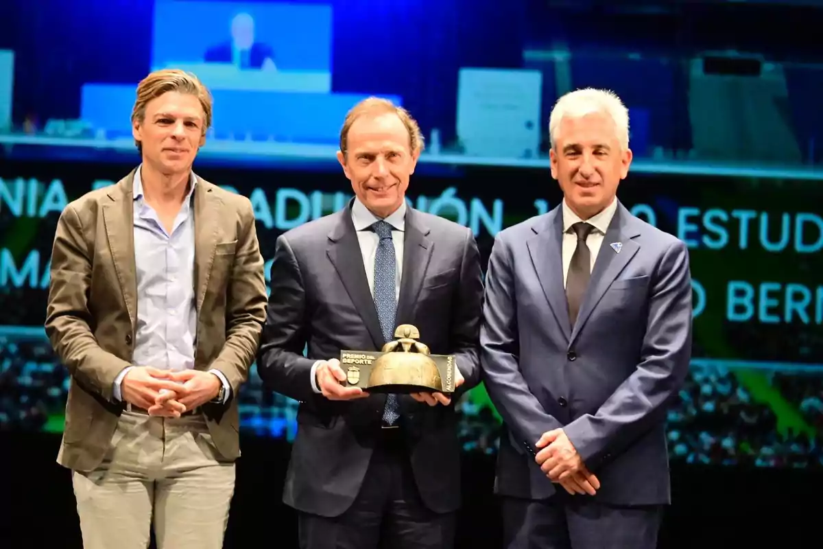 Three men pose together on a stage while one of them holds a trophy.