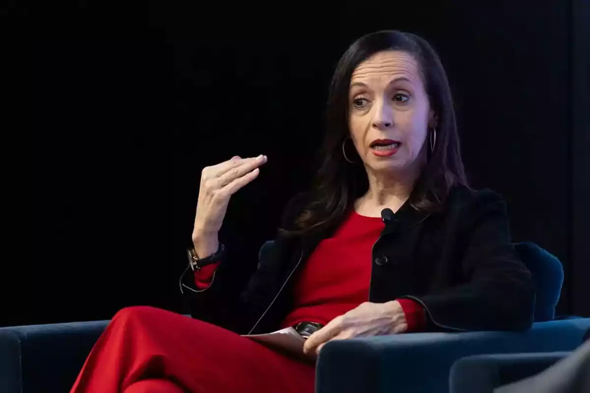 Mujer hablando en un evento, vestida de rojo y negro, gesticulando con la mano. Mujer hablando en un evento, vestida de rojo y negro, gesticulando con la mano.