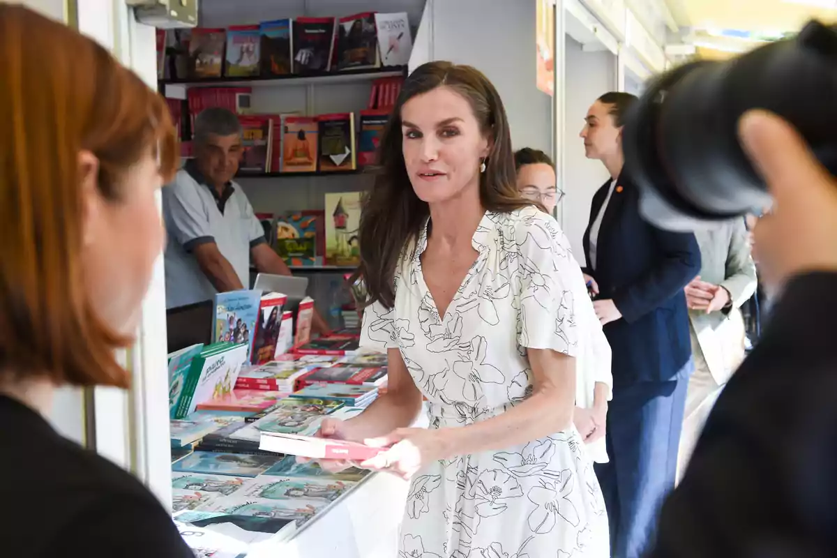 La reina Letizia con un vestido blanco con rallas negras sujetando un libro en una feria La reina Letizia con un vestido blanco con rallas negras sujetando un libro en una feria