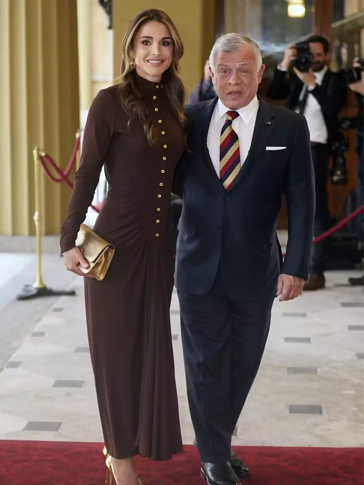 Rania of Jordan and Abdullah II elegantly dressed pose for a photo at a formal event, with photographers in the background. Rania of Jordan and Abdullah II elegantly dressed pose for a photo at a formal event, with photographers in the background.