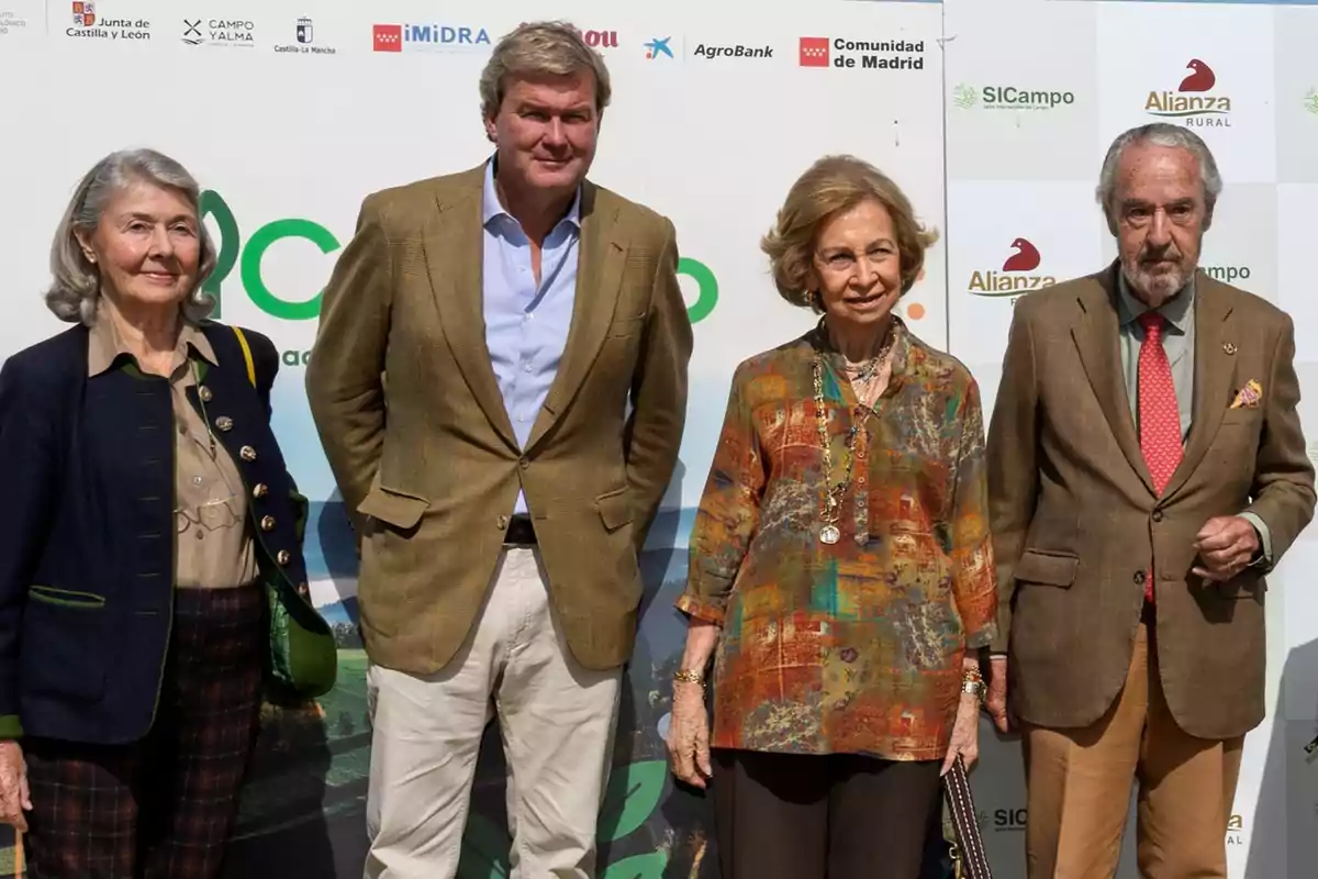 Un grupo de cuatro personas posa frente a un fondo con logotipos de varias organizaciones, todos vestidos de manera elegante y formal. Un grupo de cuatro personas posa frente a un fondo con logotipos de varias organizaciones, todos vestidos de manera elegante y formal.