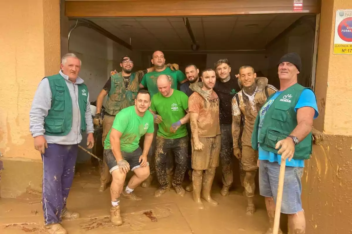 Un grupo de personas cubiertas de barro posando juntas en la entrada de un edificio.