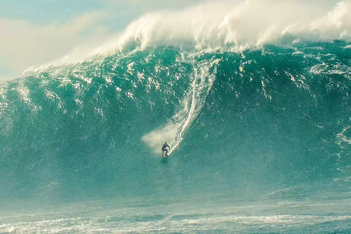 Persona surfeando una ola gigante en el océano.