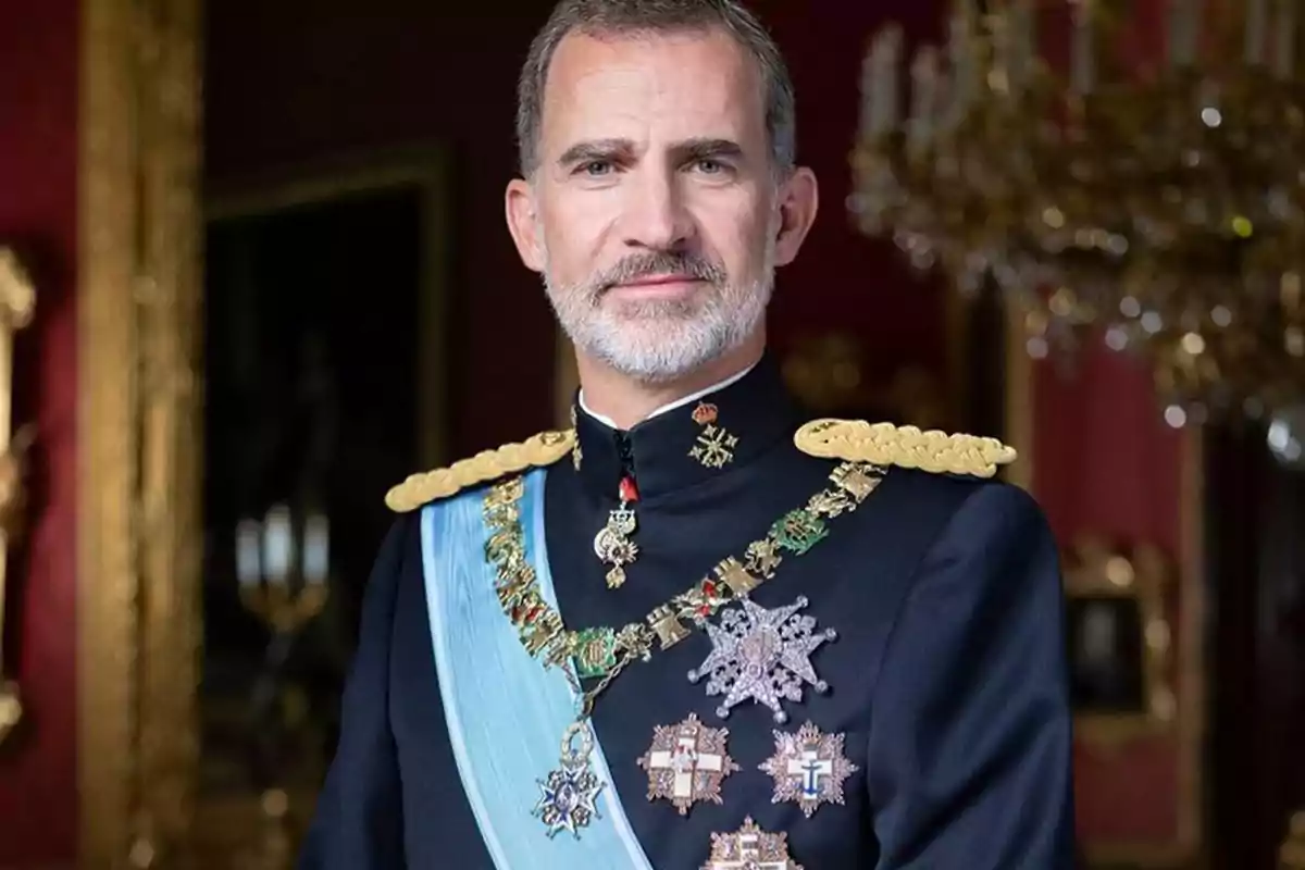 Un hombre con uniforme militar adornado con medallas y una banda azul, posando en un entorno elegante con un fondo de candelabros y marcos dorados.