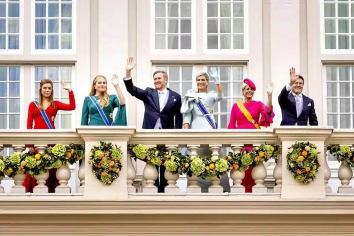 A group of elegantly dressed people waves from a balcony adorned with flower garlands, in front of a facade with large windows. A group of elegantly dressed people waves from a balcony adorned with flower garlands, in front of a facade with large windows.
