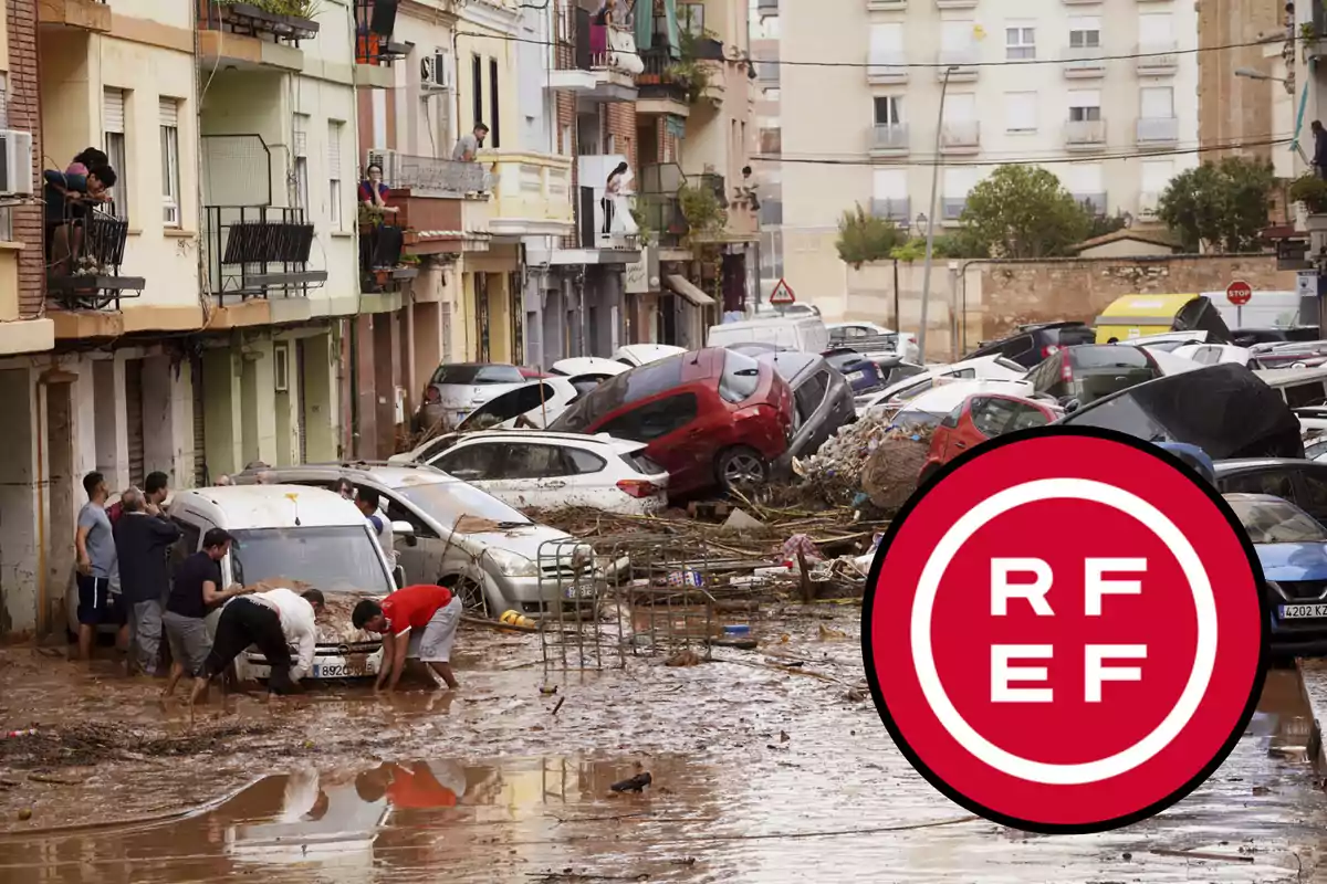 Una calle inundada con coches apilados y personas intentando mover un vehículo en medio del lodo.