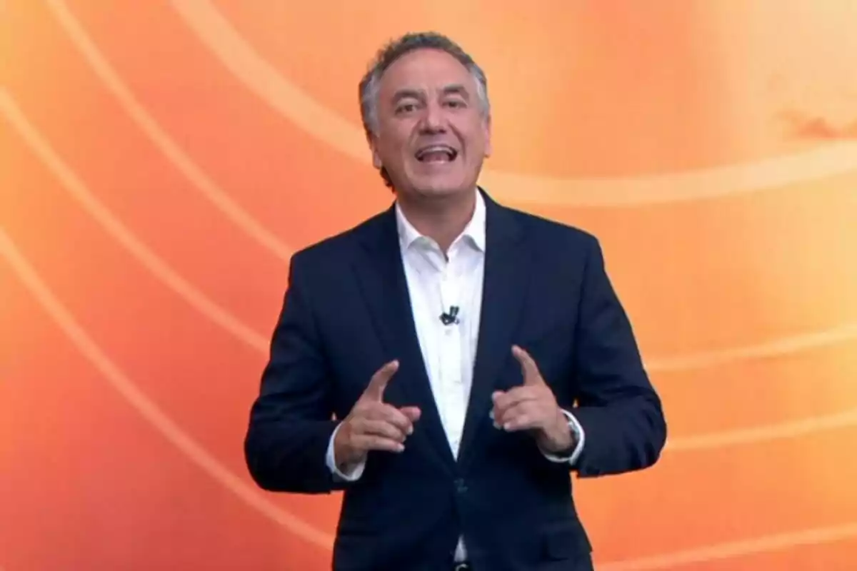 Plano medio de Roberto Brasero vestido con traje oscuro y camisa blanca hablando frente a un fondo naranja. Plano medio de Roberto Brasero vestido con traje oscuro y camisa blanca hablando frente a un fondo naranja.