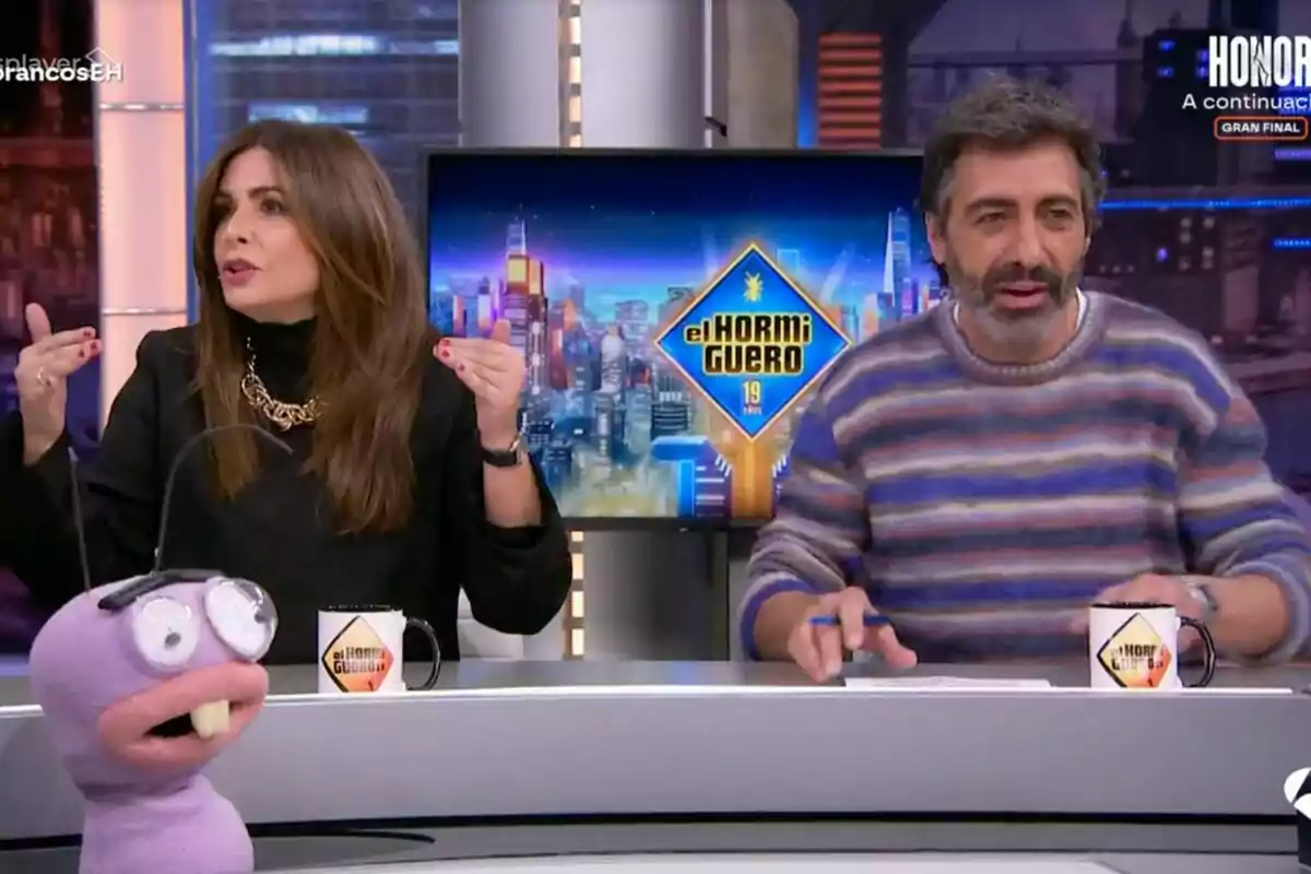 Nuria Roca y Juan del Val sentadas en un set de televisión con una marioneta y tazas con el logo de Nuria Roca y Juan del Val sentadas en un set de televisión con una marioneta y tazas con el logo de