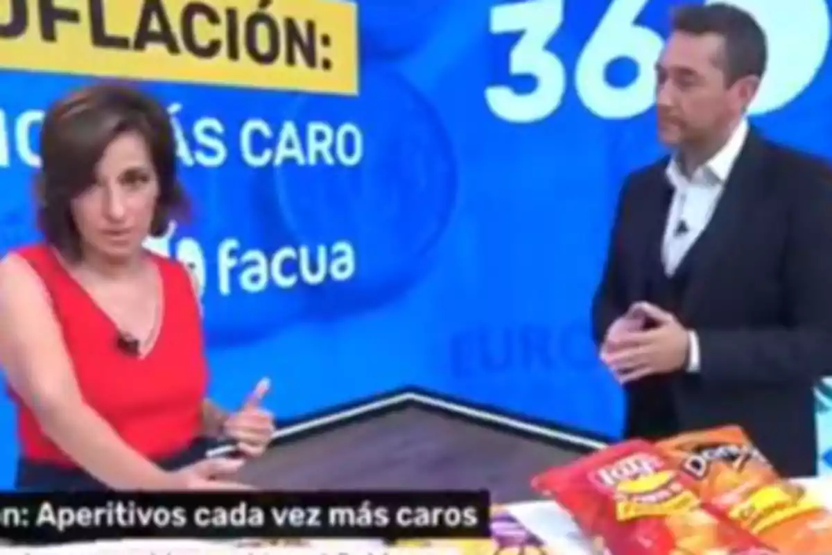 Dos presentadores de televisión conversan en un estudio con fondo azul y productos de botanas sobre una mesa, mientras en pantalla se muestra información sobre el aumento de precios de los aperitivos. Dos presentadores de televisión conversan en un estudio con fondo azul y productos de botanas sobre una mesa, mientras en pantalla se muestra información sobre el aumento de precios de los aperitivos.