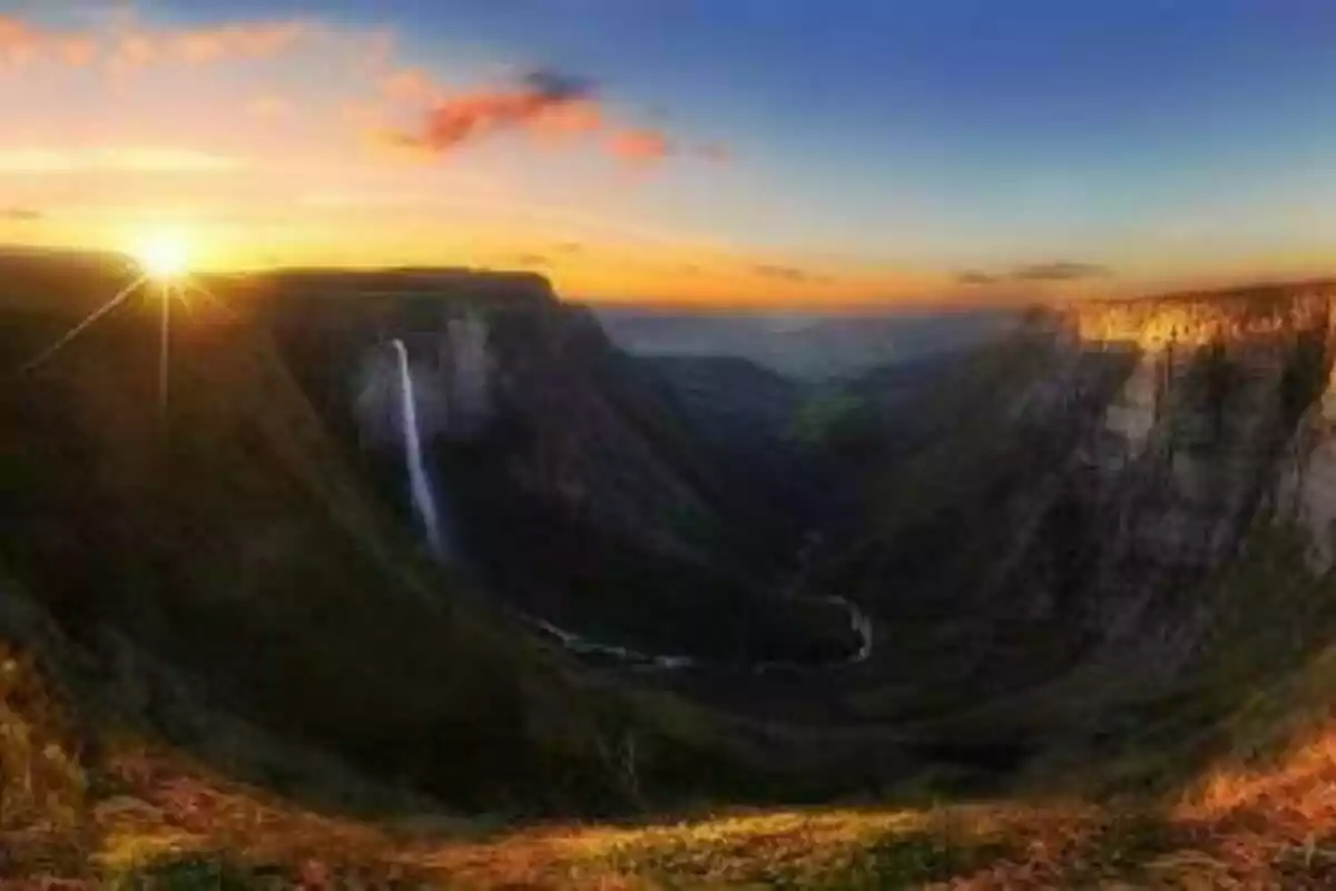 Atardecer en un valle con una cascada y montañas al fondo.