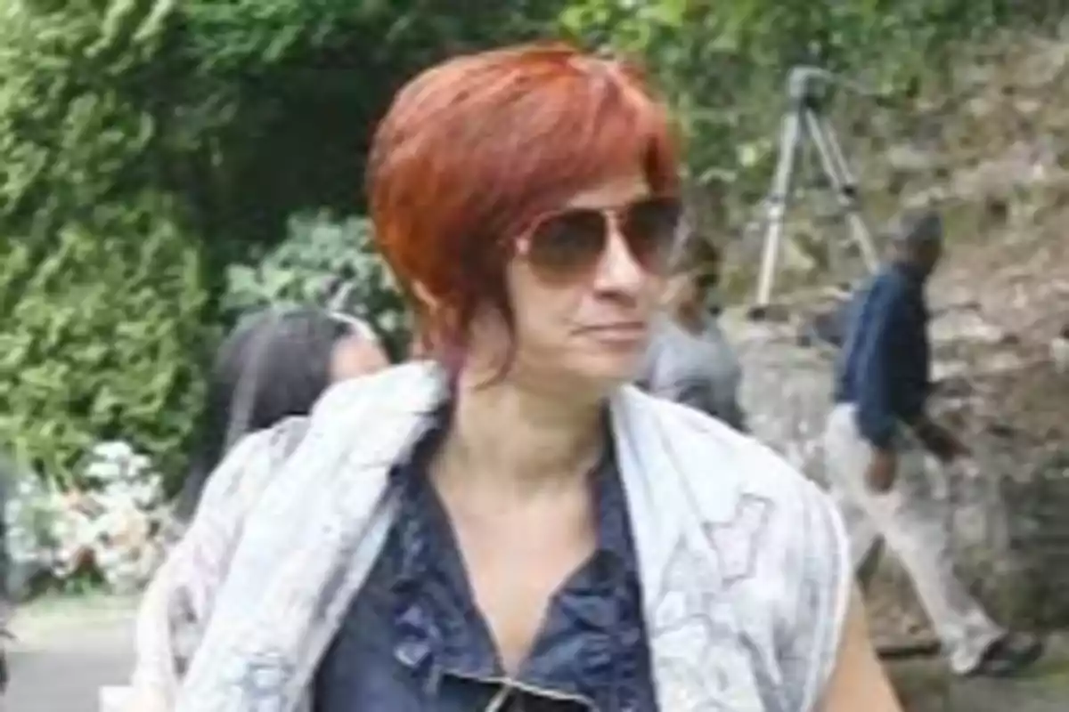 Mujer con cabello corto y gafas de sol en un entorno al aire libre con vegetación. Mujer con cabello corto y gafas de sol en un entorno al aire libre con vegetación.