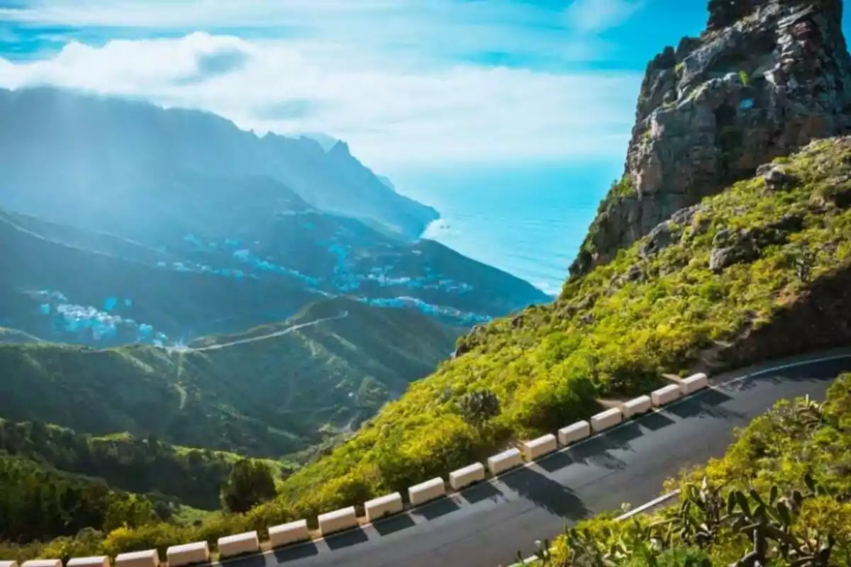 Carretera sinuosa en una montaña con vista al mar y un pueblo en el valle.