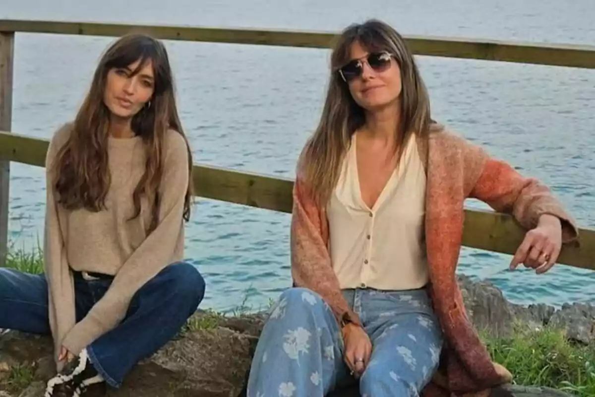Dos mujeres -que son Sara Carbonero e Isabel Jiménez- sentadas al aire libre frente al mar, una lleva un suéter beige y la otra un cárdigan naranja, ambas con cabello largo y suelto. Dos mujeres -que son Sara Carbonero e Isabel Jiménez- sentadas al aire libre frente al mar, una lleva un suéter beige y la otra un cárdigan naranja, ambas con cabello largo y suelto.