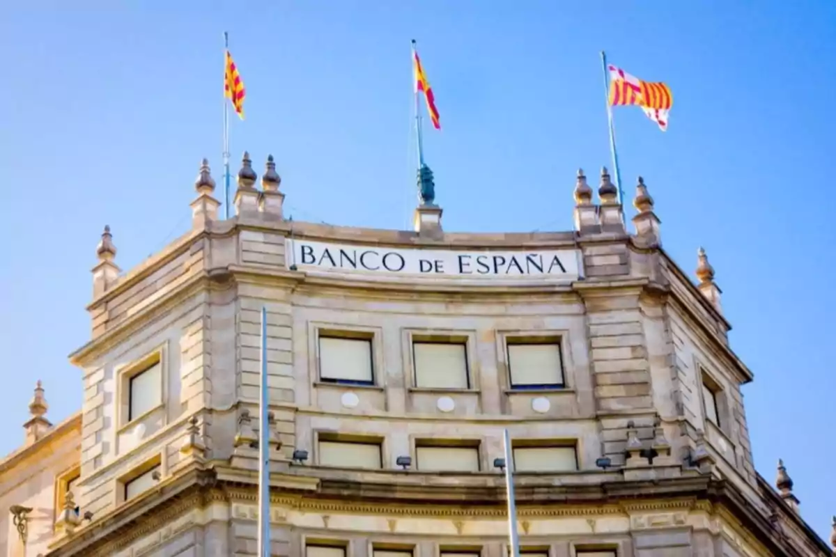 Fachada del edificio del Banco de España con banderas ondeando en la parte superior y cielo despejado de fondo Fachada del edificio del Banco de España con banderas ondeando en la parte superior y cielo despejado de fondo